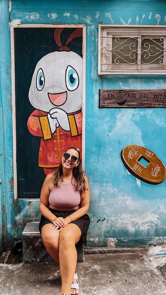 Talat Noi cute murals Ale sitting on the stairs to get a picture Ale positing for a photo in one of the iconic alleys of Talat Noi. Spotting cute murals in Talat Noi Bangkok - Ale sitting on the steps outside the door