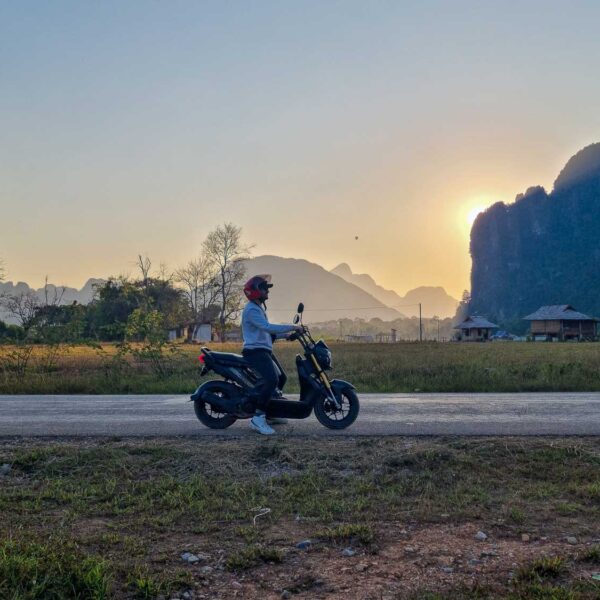 Toti driving a scooter with an amazing view of Vang Vieng landscape at the back | Is Vang Vieng worth visiting