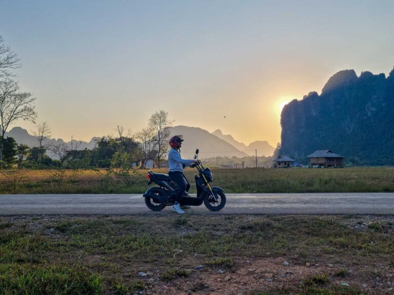 Toti driving a scooter with an amazing view of Vang Vieng landscape at the back | Is Vang Vieng worth visiting