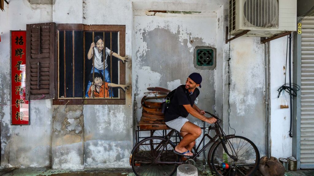 Toti sitting on a bike and having the street murals behind in Georgetown Penang