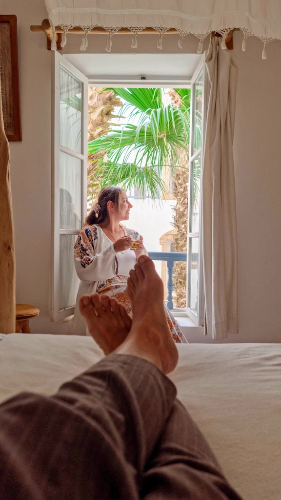 Ale sitting by the window drinking a tea while Toti is relaxing on the bed 