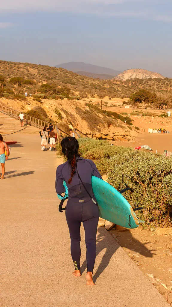 Best Surfing spots in Taghazout -  A surfer in Morocco reaching the beach through the pedestrian path from one beach to another.