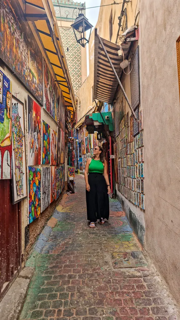 Vertical shot of the Rainbow Alley in Fes medina featuring colourful street art and carpets hanging on walls.