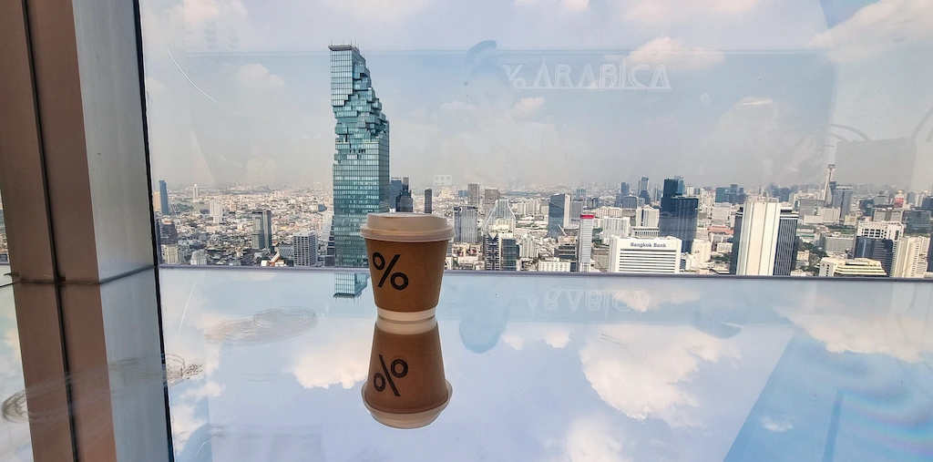 The cup of Arabica seems floating on the glass on the 55th floor of Empire tower in Bangkok, looking at the Mahanahkon building